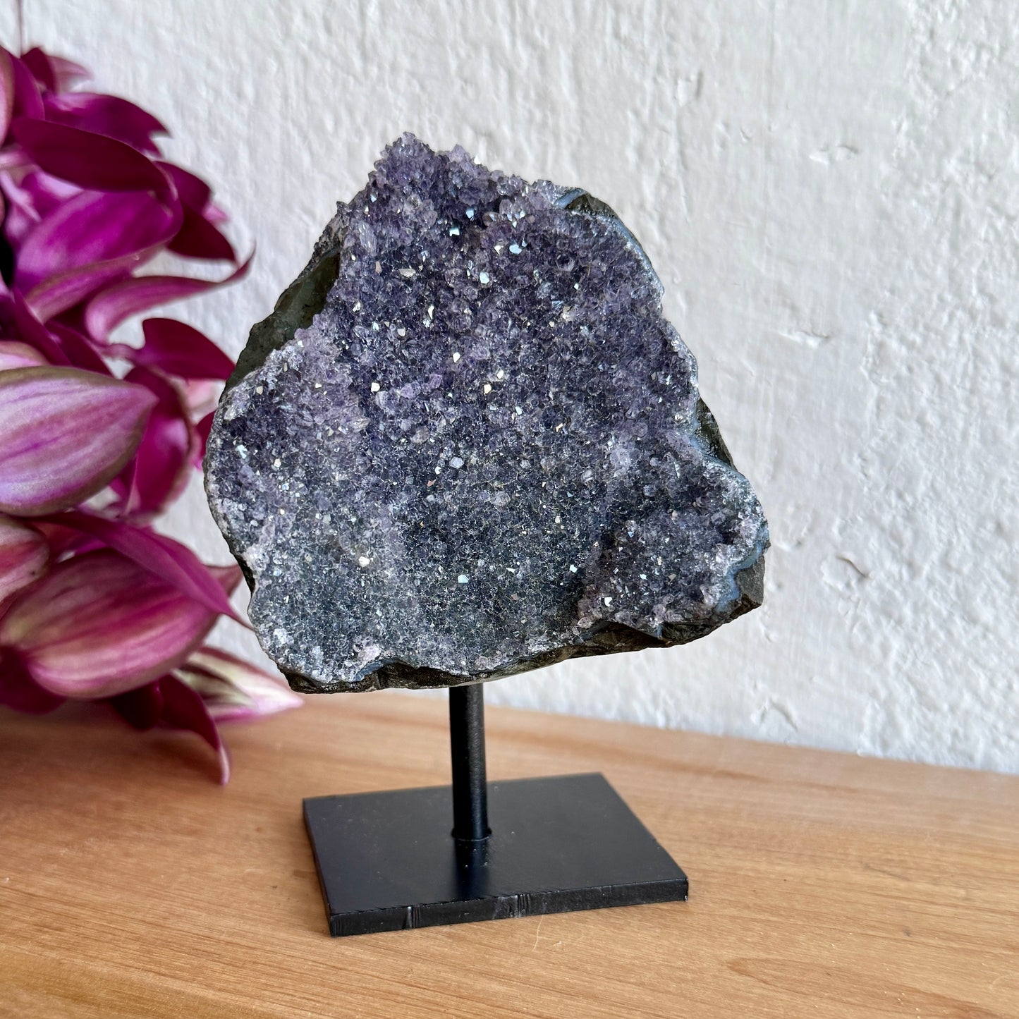 Geode amethyst crystal on a stand with pink flowers in the background