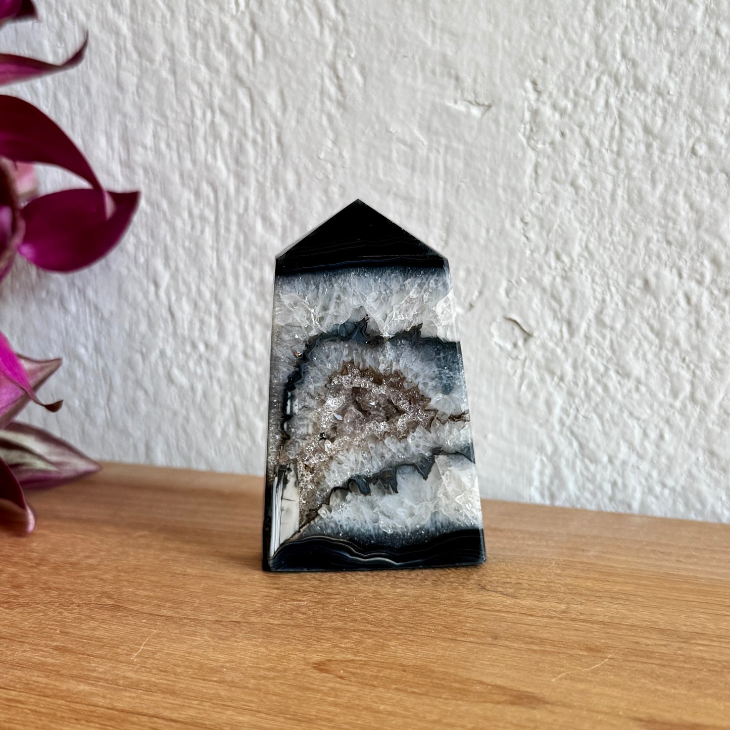 Black sardonyx agate crystal tower on a wooden surface with a white wall background