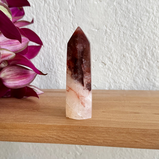 Hematoid crystal tower on a wooden surface with a white wall and purple flowers in the background