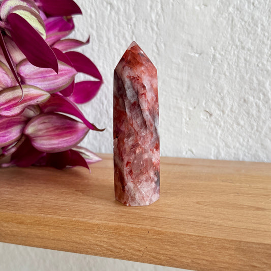 Hematoid quartz red crystal tower on a wooden surface with a white wall background