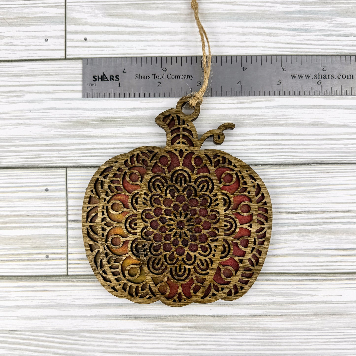 Geometric pumpkin suncatcher made from wood and acrylic lying flat with a ruler showing the approximate width.