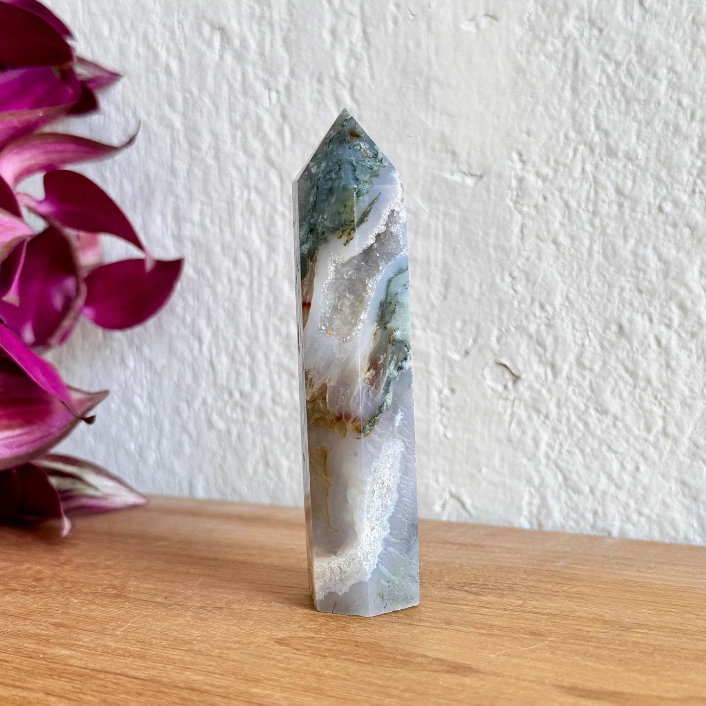 Moss agate crystal tower on a wooden surface with a white wall background