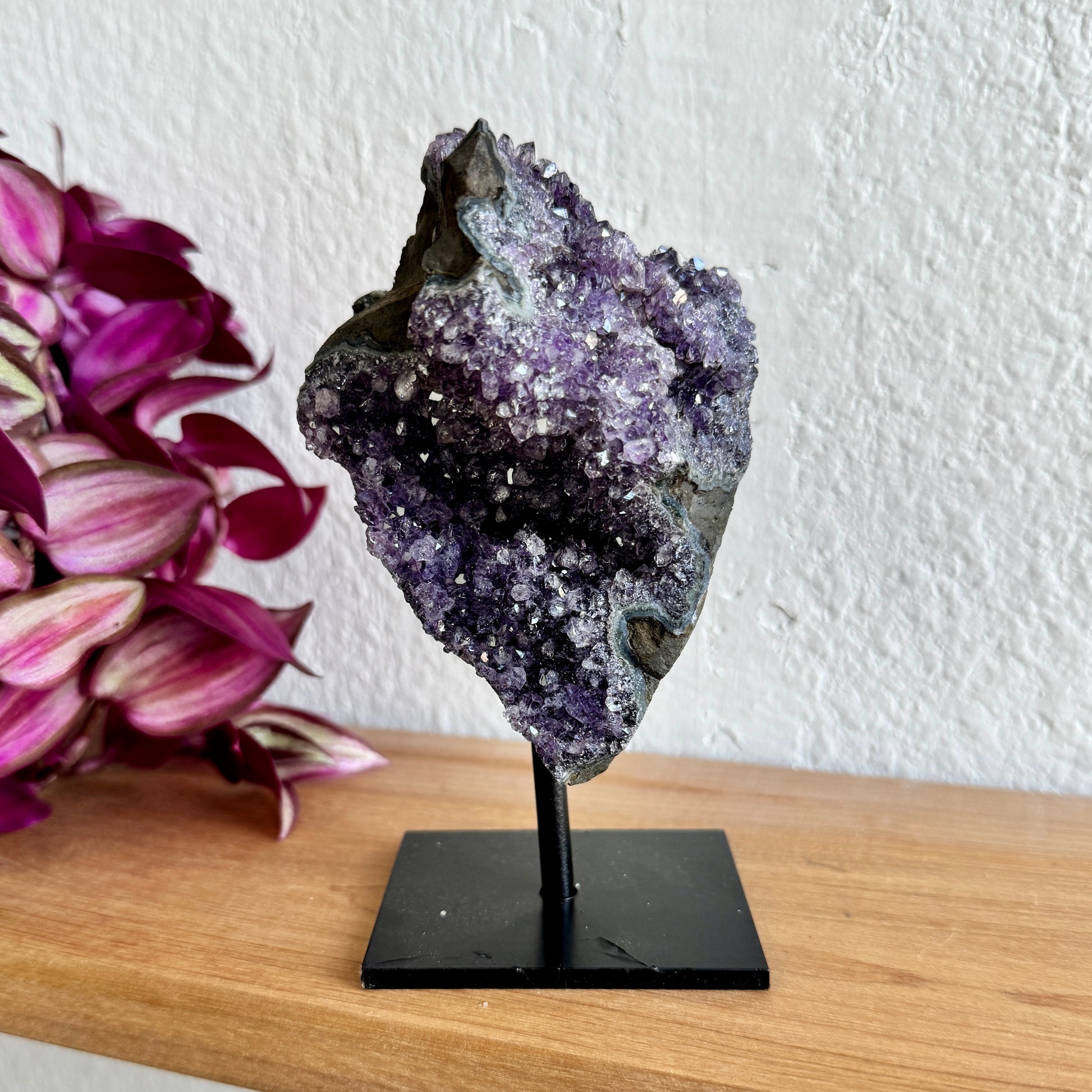 Amethyst crystal on a stand with pink flowers in the background