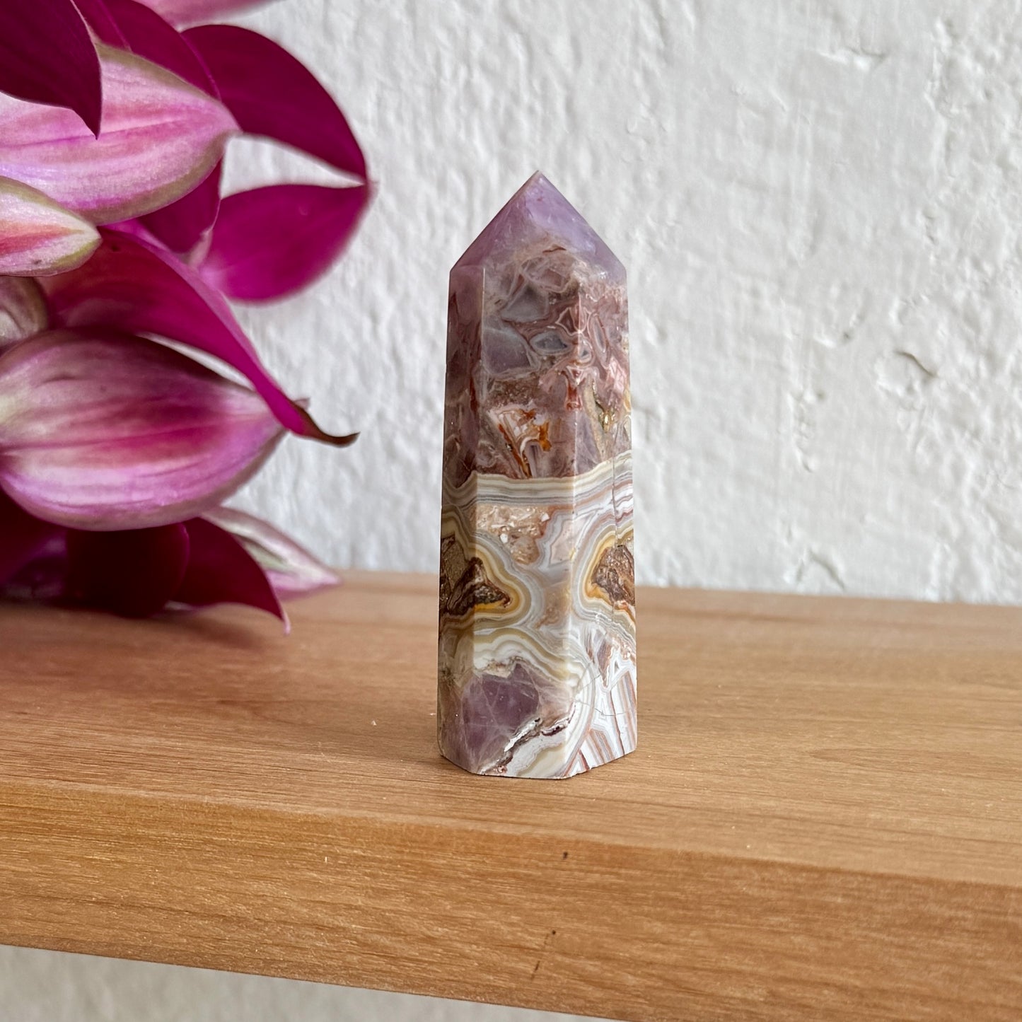 Amethyst agate crystal tower on a wooden surface with pink flowers in the background