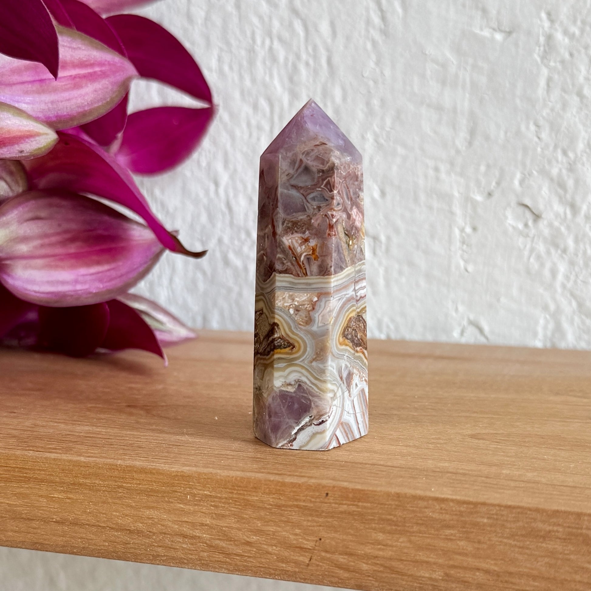 Amethyst agate crystal tower on a wooden surface with pink flowers in the background
