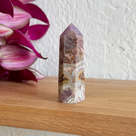 Amethyst agate crystal tower on a wooden surface with pink flowers in the background