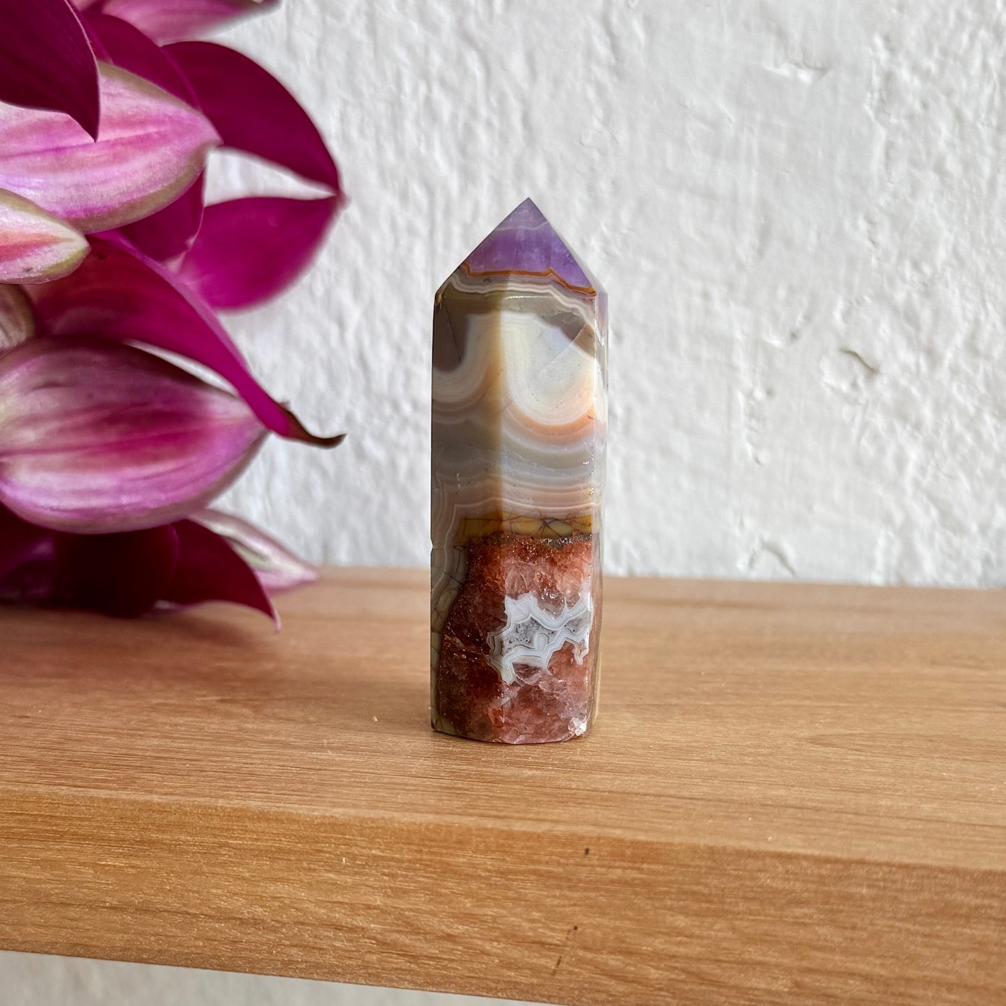 Amethyst agate tower on a wooden surface with pink flowers in the background
