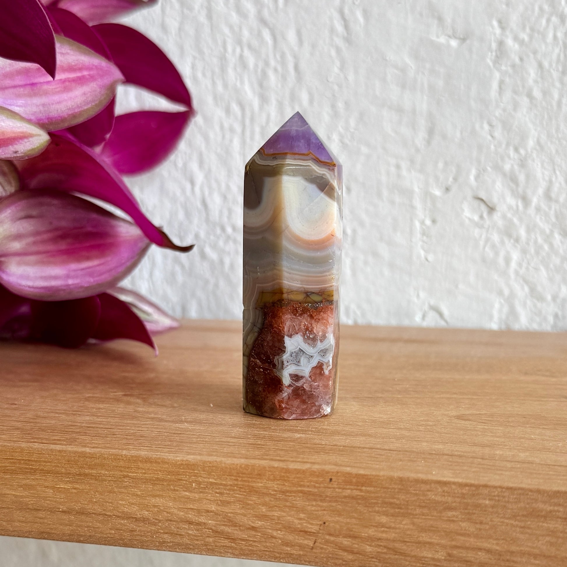 Amethyst agate tower on a wooden surface with pink flowers in the background