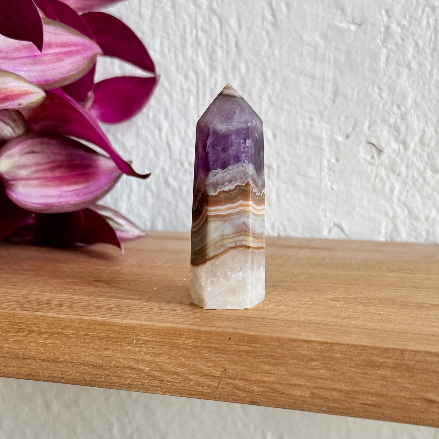 Decorative amethyst agate crystal on a wooden surface with pink flowers in the background