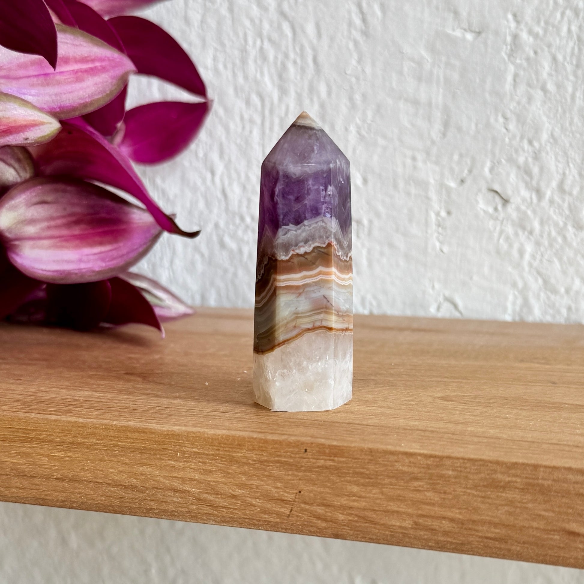 Decorative amethyst agate crystal on a wooden surface with pink flowers in the background