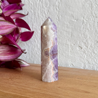 Amethyst agate crystal tower on a wooden surface with pink flowers in the background