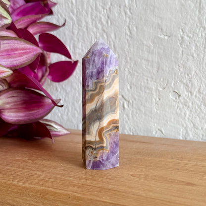 Amethyst agate crystal on a wooden surface with pink flowers in the background