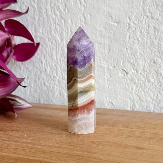 Multicolored amethyst agate crystal tower on a wooden surface with a white wall background