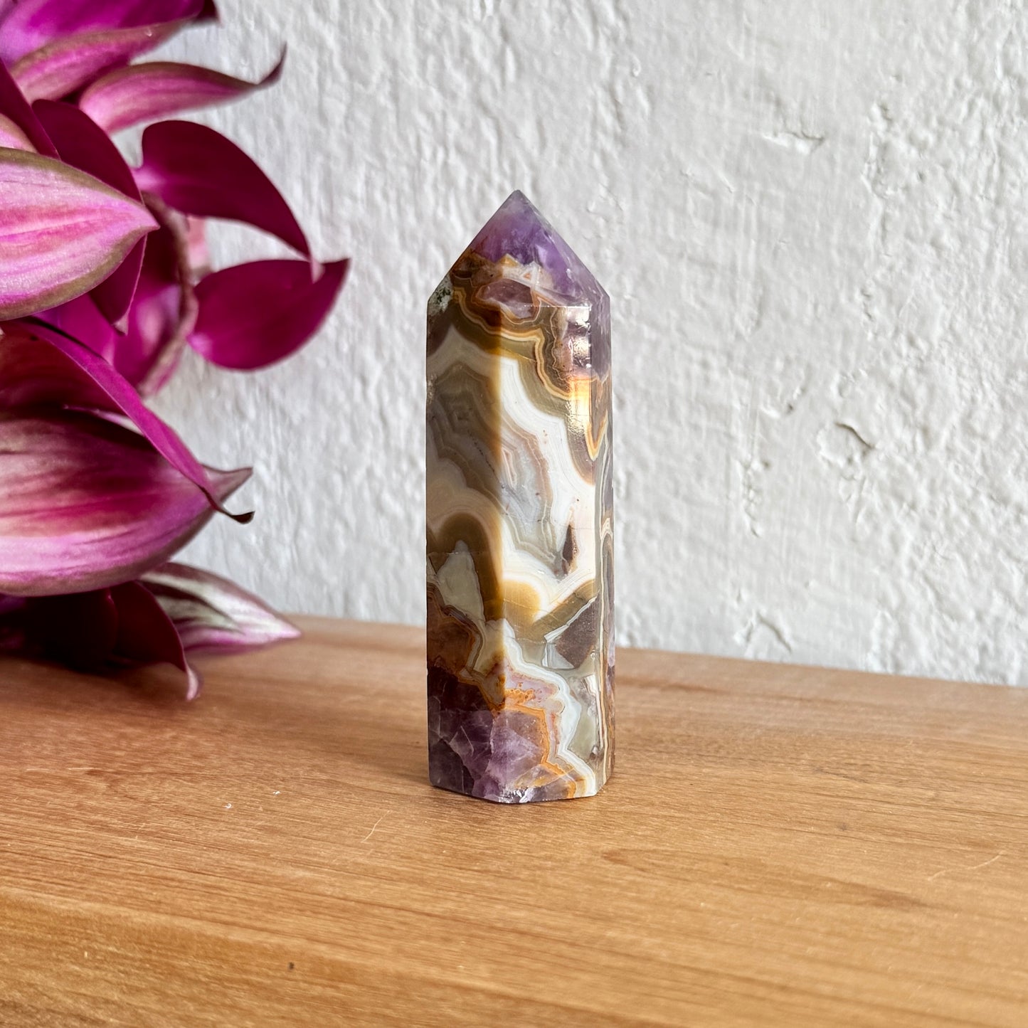 Decorative amethyst agate crystal on a wooden surface with pink flowers in the background