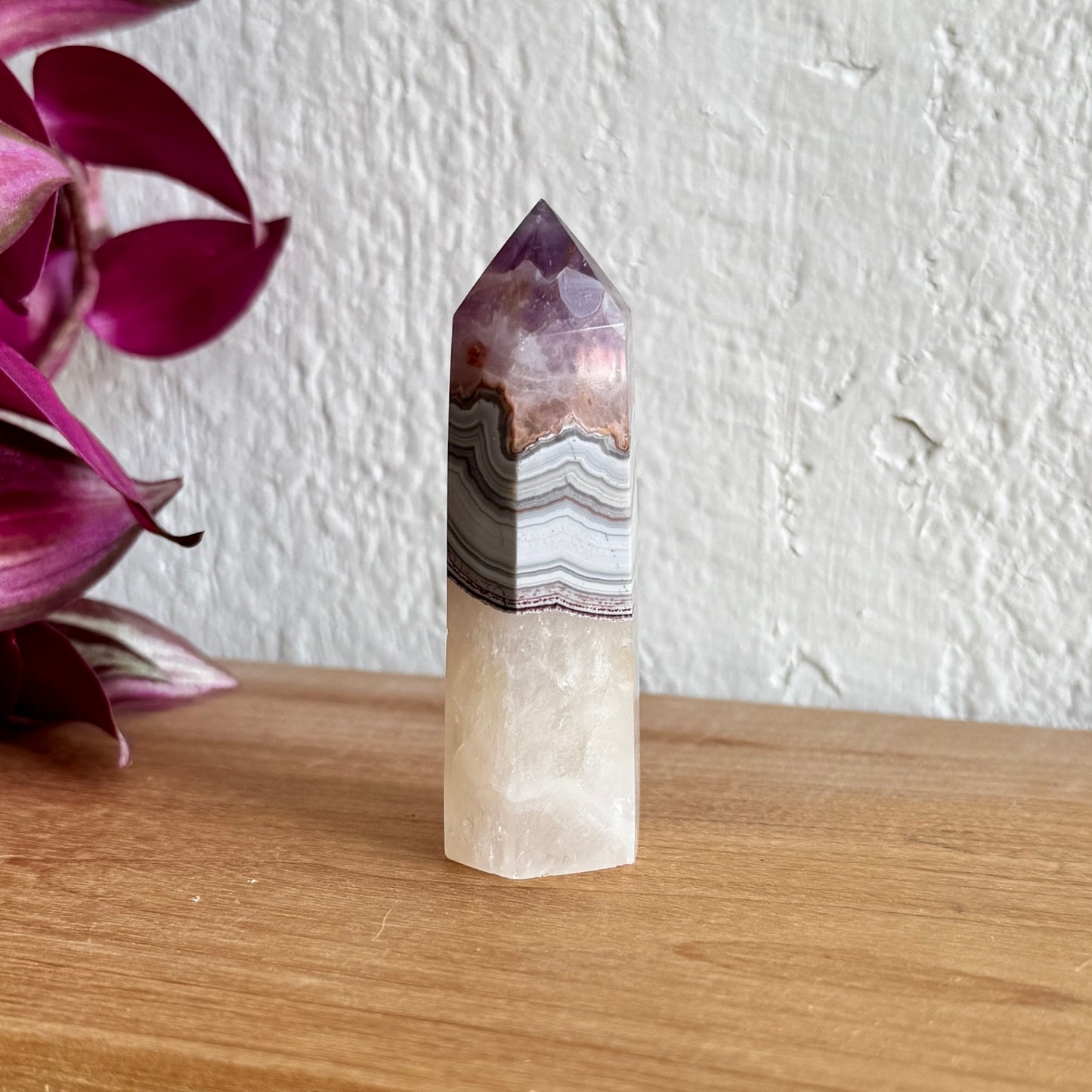 Amethyst agate crystal tower with purple and white patterns on a wooden surface with a white wall background
