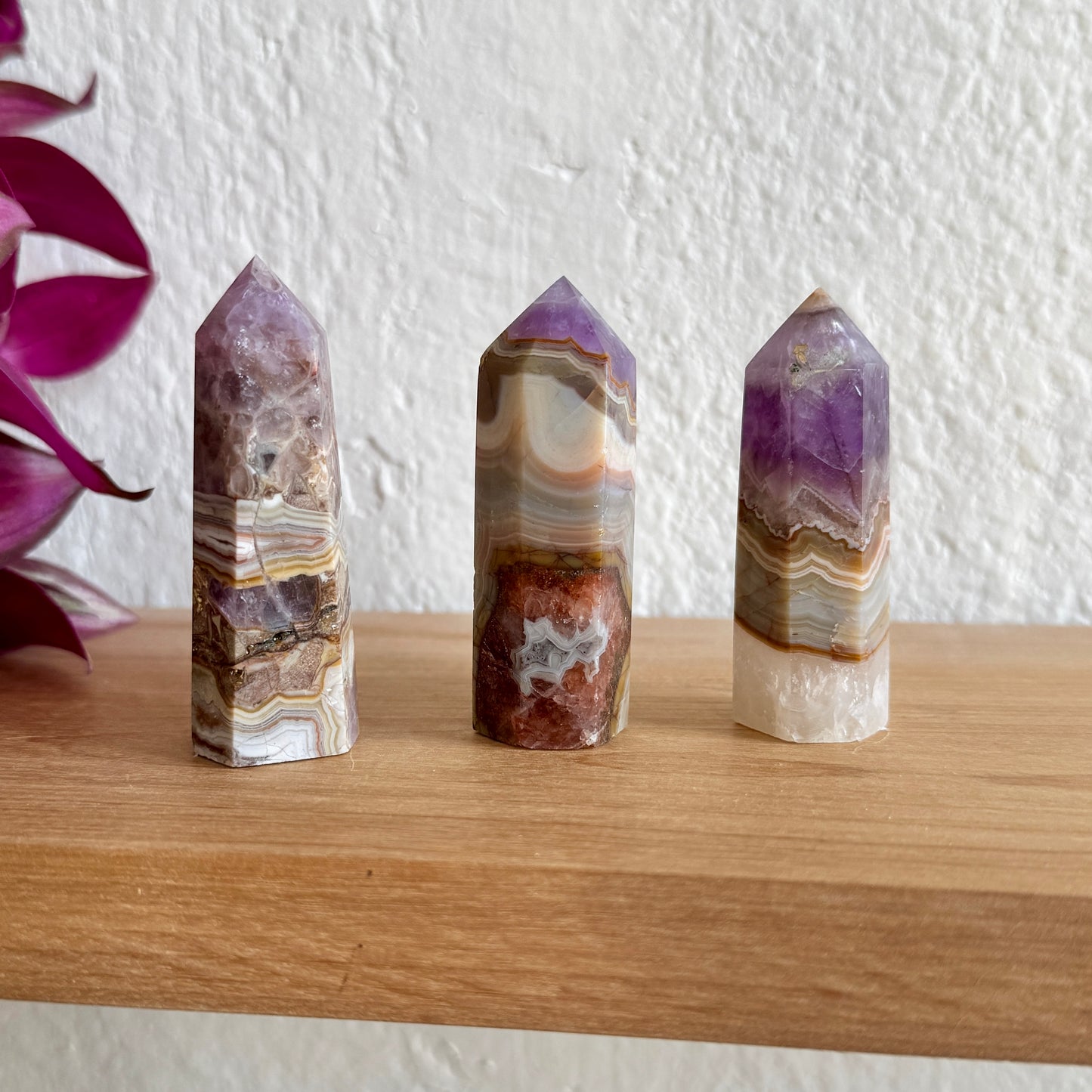 Three amethyst agate crystal towers on a wooden surface with a white wall background