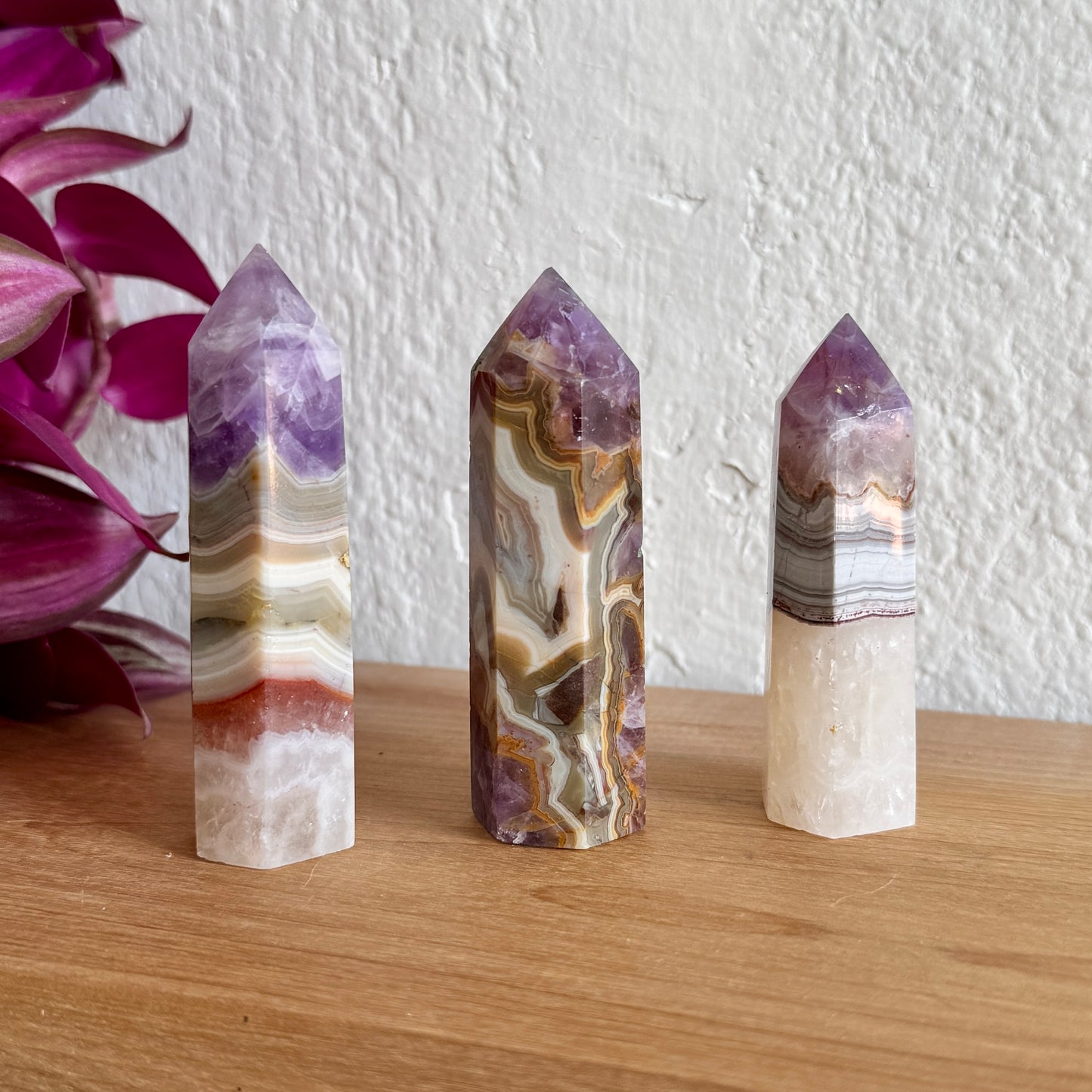 Three amethyst agate crystal towers on a wooden surface with a white wall and purple flowers in the background
