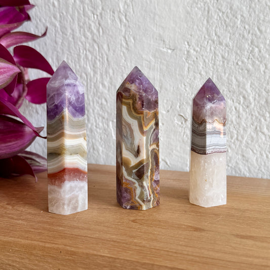 Three amethyst agate crystal towers on a wooden surface with a white wall and purple flowers in the background