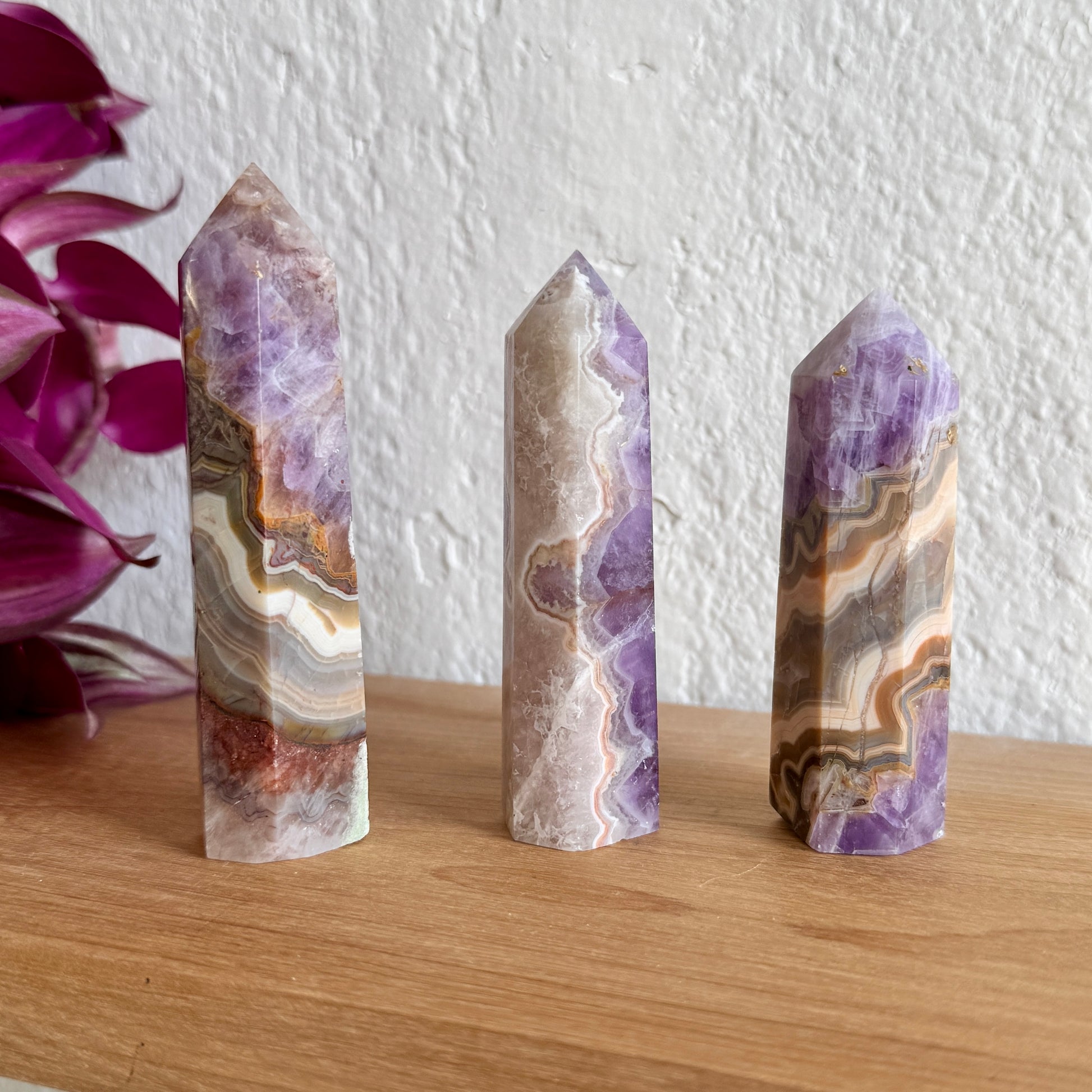 Three amethyst agate crystal towers with purple and brown patterns on a wooden surface with a white wall background.