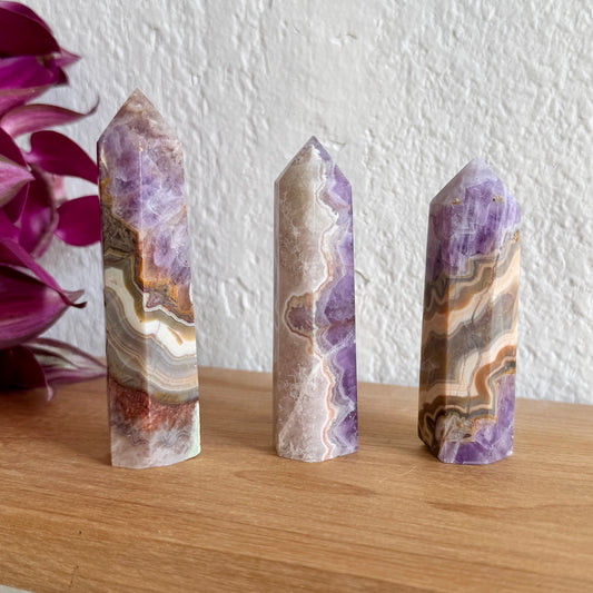 Three amethyst agate crystal towers with purple and brown patterns on a wooden surface with a white wall background.