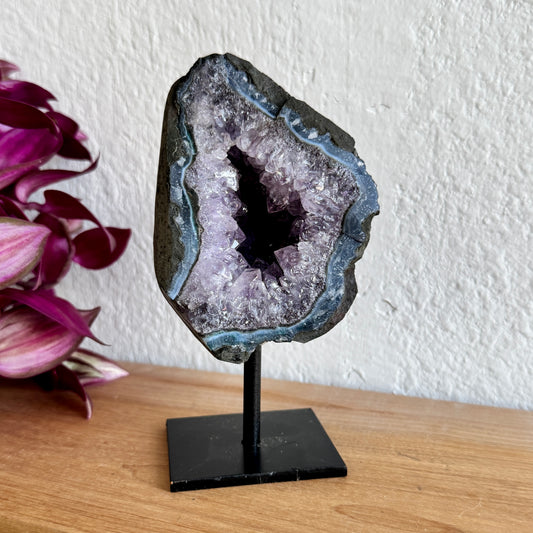 Geode amethyst crystal on a stand with pink flowers in the background