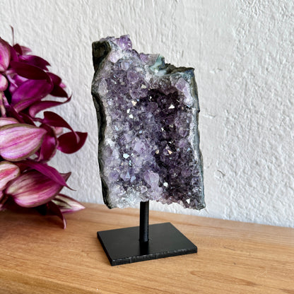 Amethyst crystal on a stand with pink flowers in the background