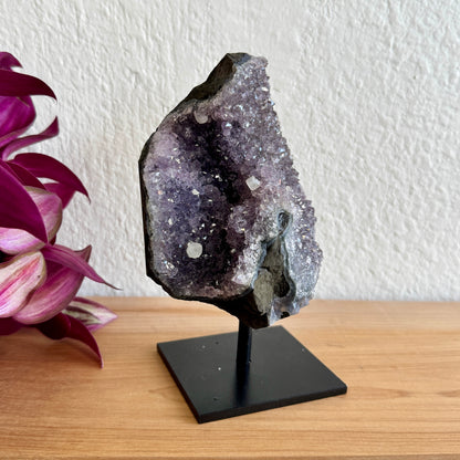 Amethyst crystal on a stand with a pink flower in the background