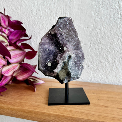 Geode amethyst crystal on a stand with pink flowers in the background