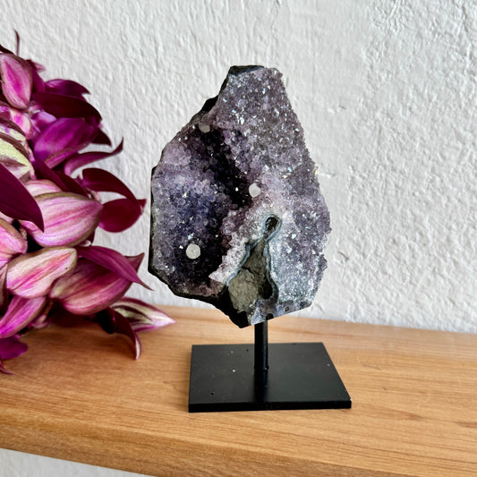 Geode amethyst crystal on a stand with pink flowers in the background