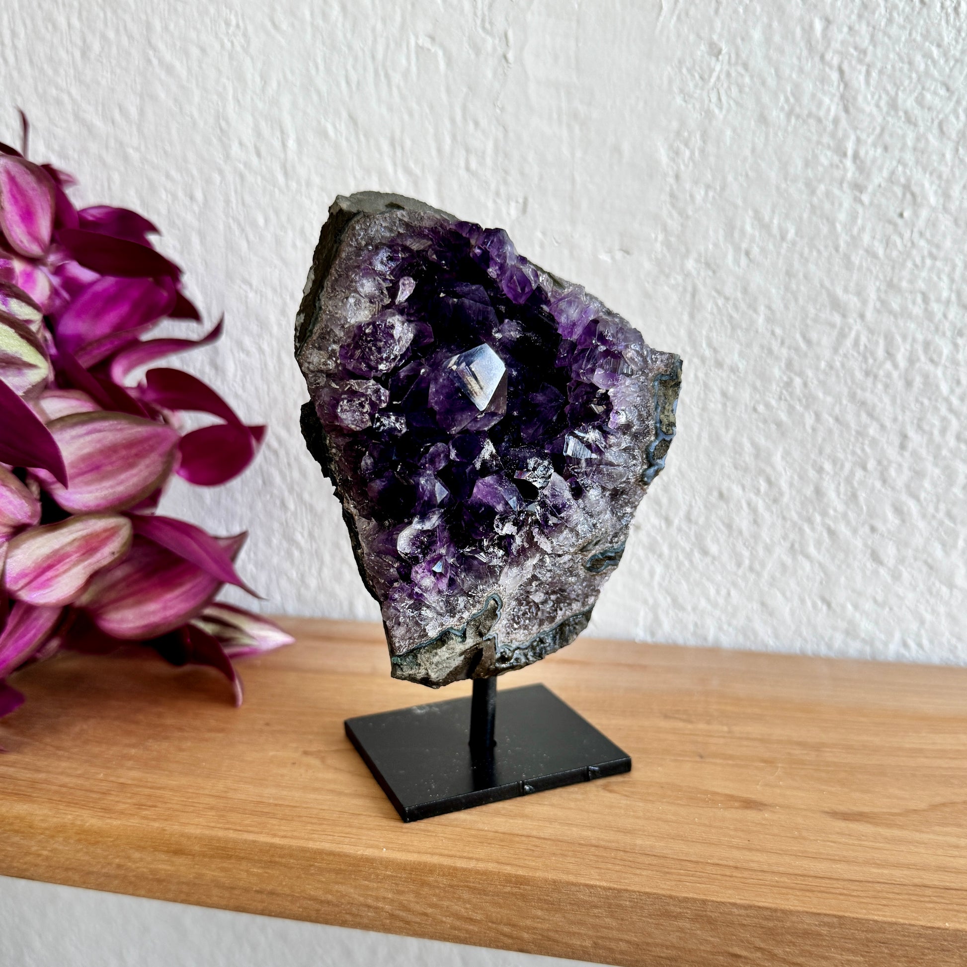 Amethyst crystal on a stand with pink flowers in the background