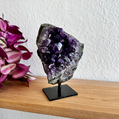 Amethyst crystal on a stand with pink flowers in the background