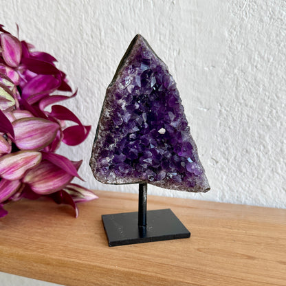 Amethyst crystal on a stand with pink flowers in the background