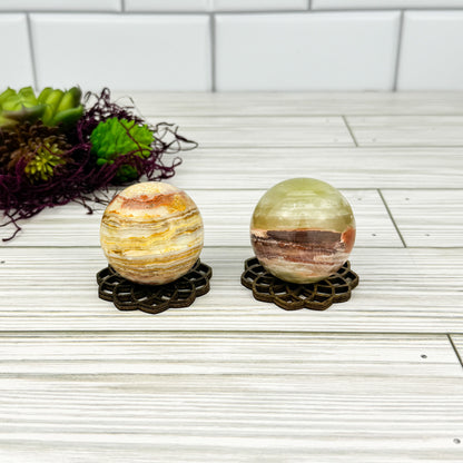 Two decorative banded calcite spheres on wood stands with a white tiled background