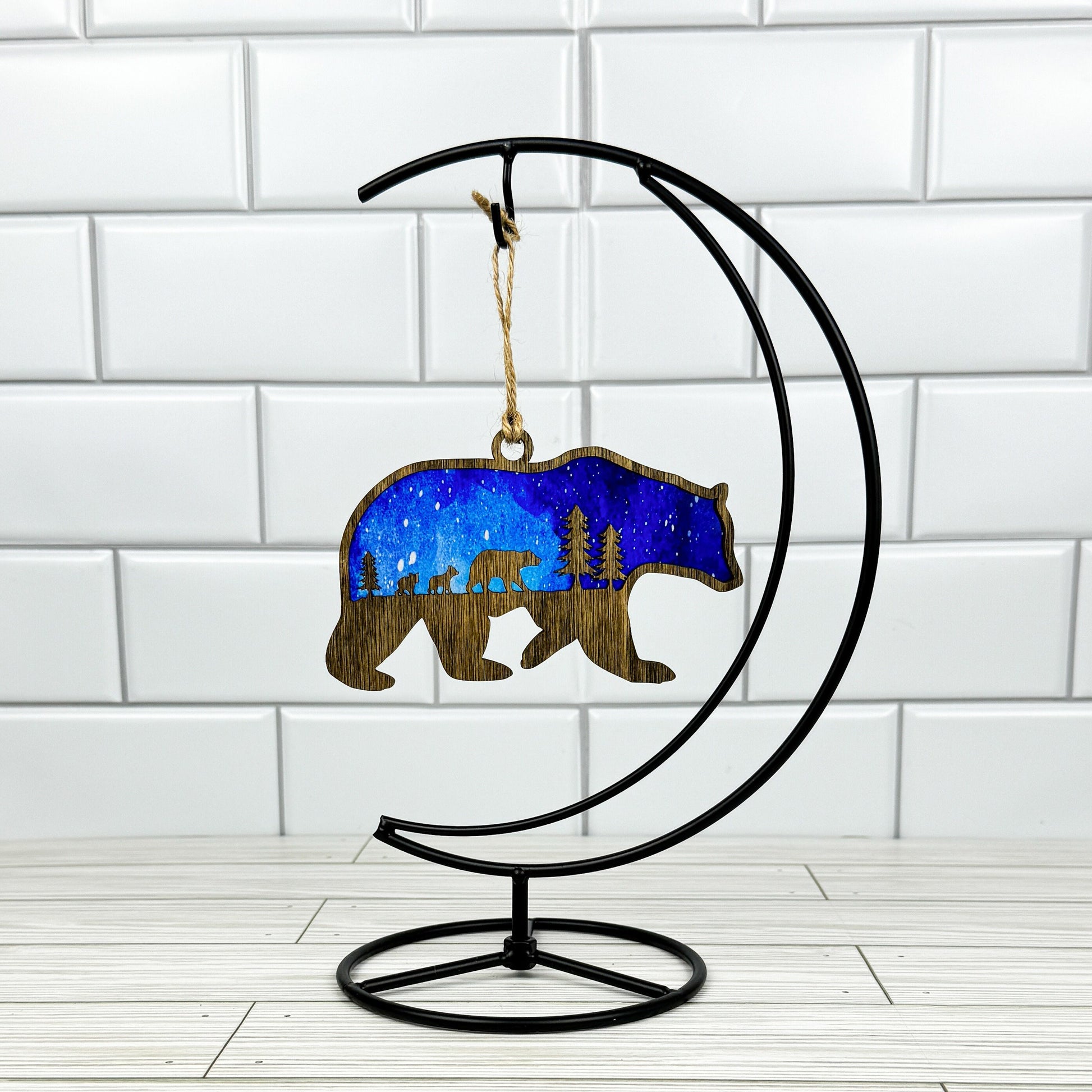 Bear suncatcher made from dark stained wood and acrylic hanging on a metal stand in front of a white tiled wall.