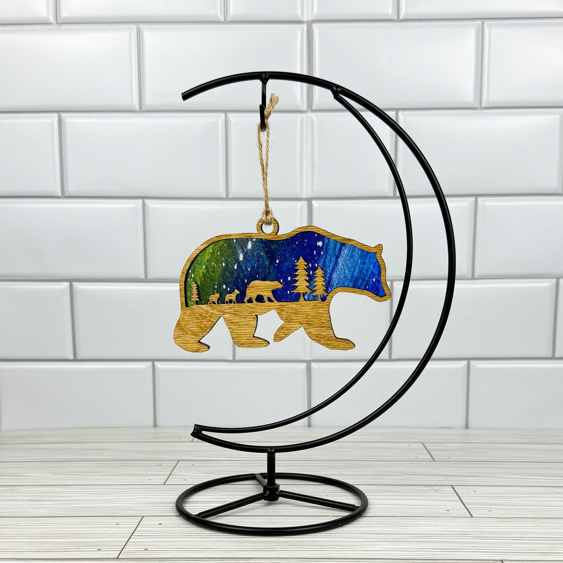 Bear suncatcher made from light stained wood and acrylic hanging on a metal stand in front of a white tiled wall.