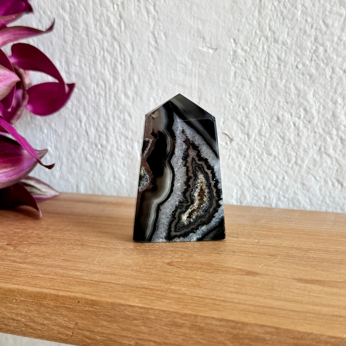 Black and white agate tower on a wooden surface with a white wall and purple flowers in the background