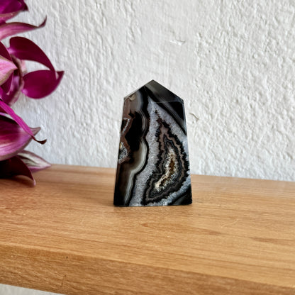 Black and white agate tower on a wooden surface with a white wall and purple flowers in the background
