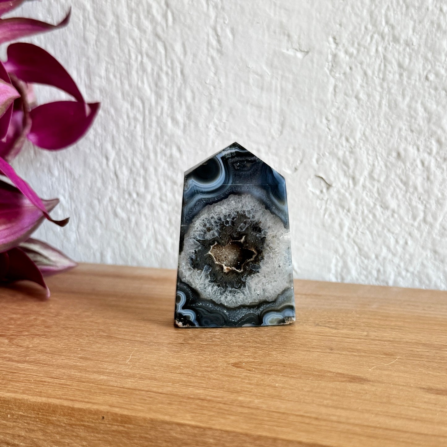 Sardonyx crystal on a wooden surface with a white wall and pink flowers in the background