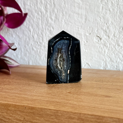 Black sardonyx crystal on a wooden surface with a white wall background