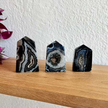 Three banded agate crystal towers on a wooden surface with a white wall background