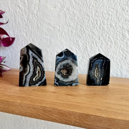 Three banded agate crystal towers on a wooden surface with a white wall background