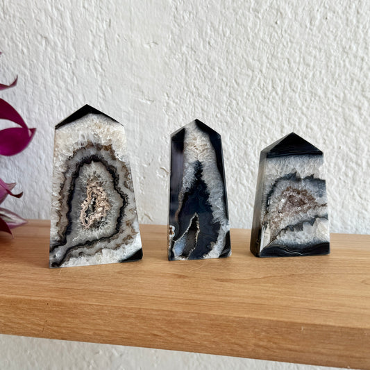 Three black sardonyx crystal towers on a wooden shelf with a white wall background