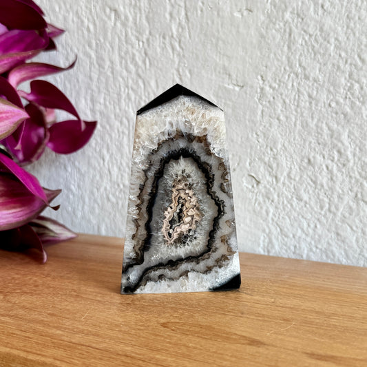 Banded agate crystal on a wooden surface with a white wall and purple flowers in the background