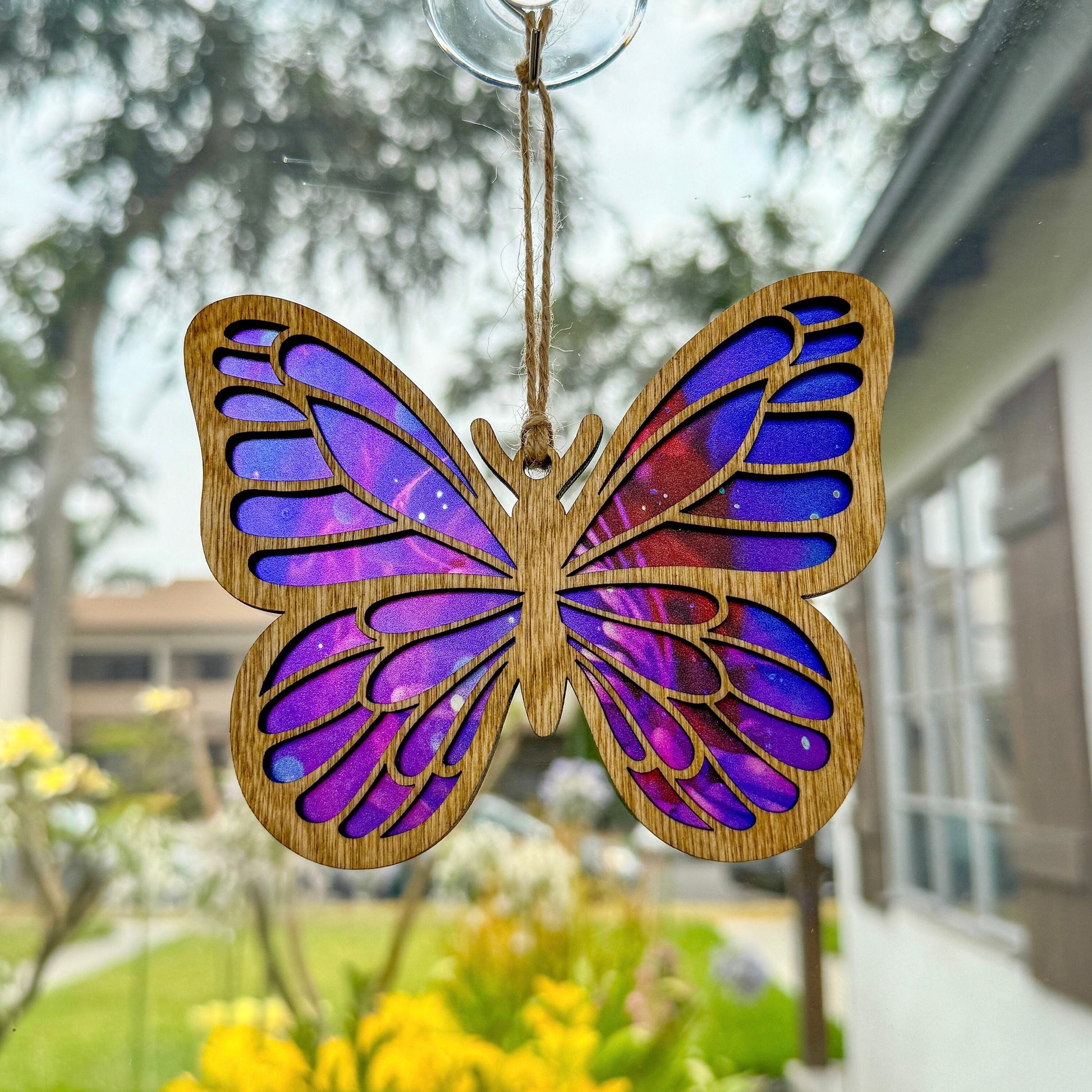 Butterfly suncatcher made from wood and acrylic hanging in window shown in the light stain option.