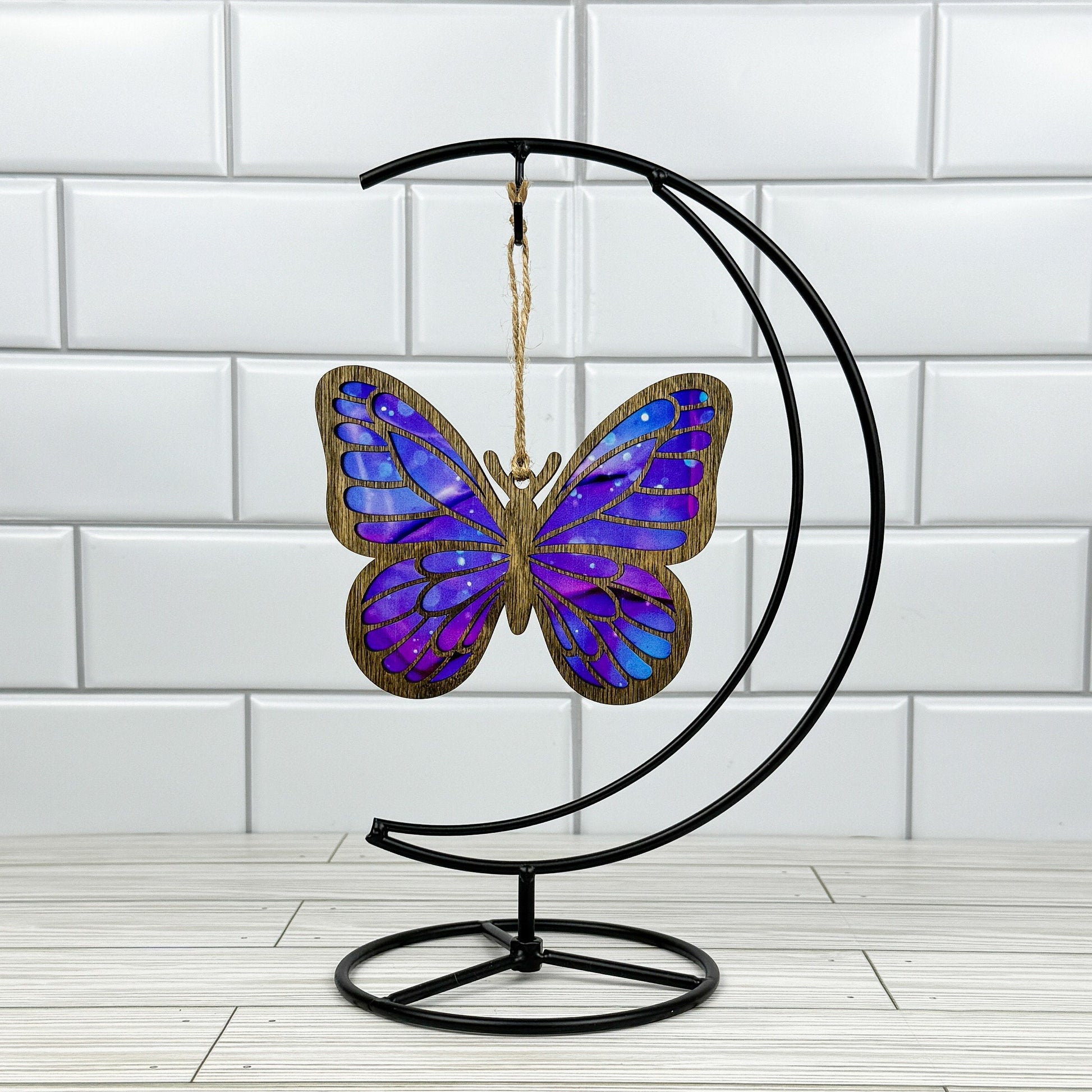 Butterfly suncatcher made from wood and acrylic shown in dark stain option hanging on a metal stand in front of a white tiled wall.