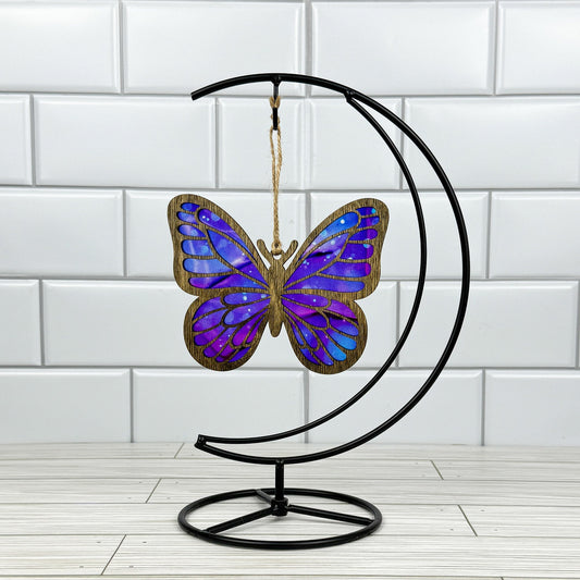 Butterfly suncatcher made from wood and acrylic shown in dark stain option hanging on a metal stand in front of a white tiled wall.