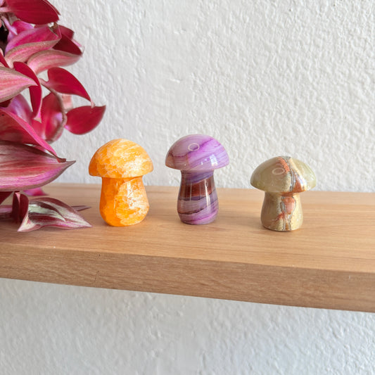 Three colorful mushroom-shaped crystal carvings on a wooden shelf.