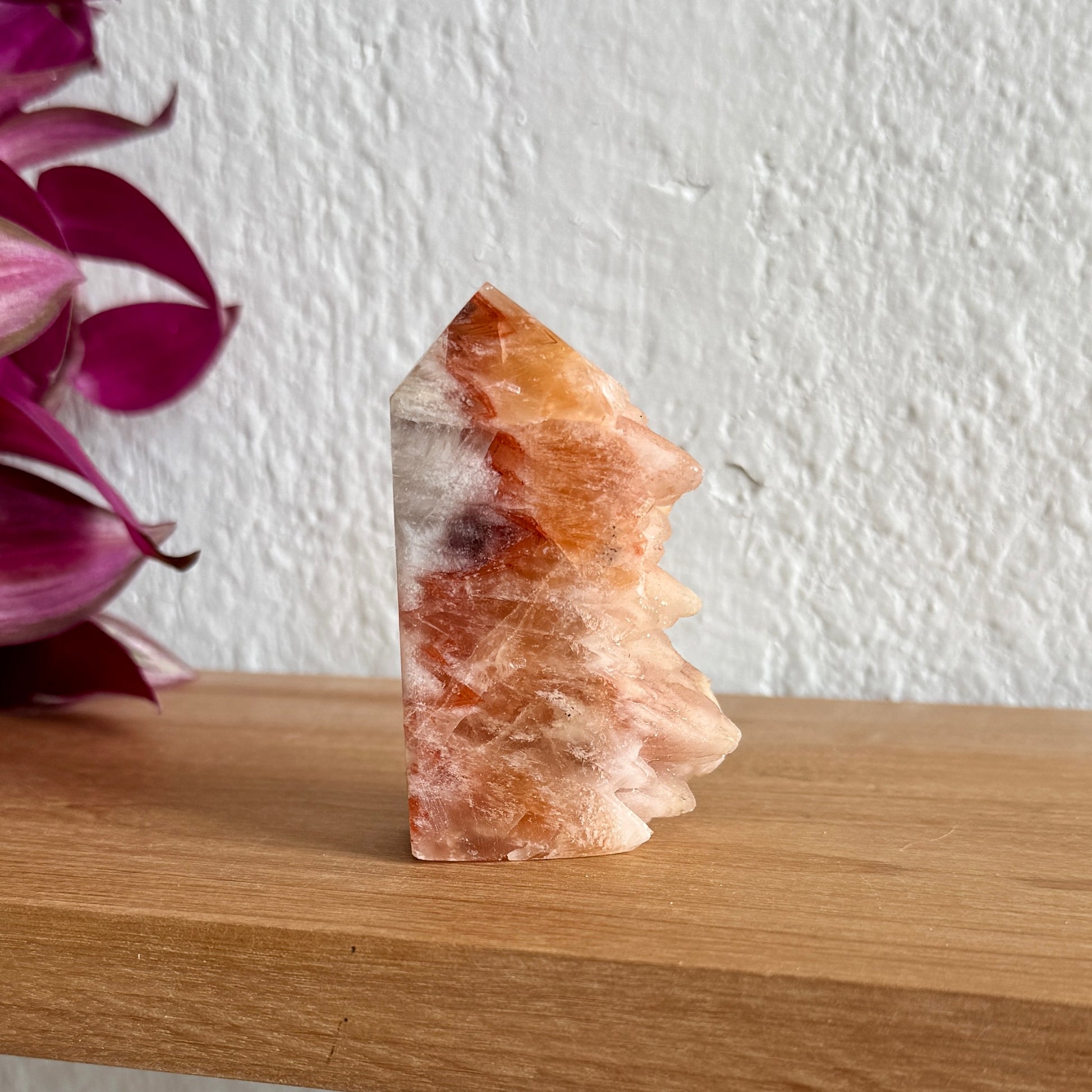 Dogtooth calcite crystal tower on a wooden surface with a white wall and purple plant in the background