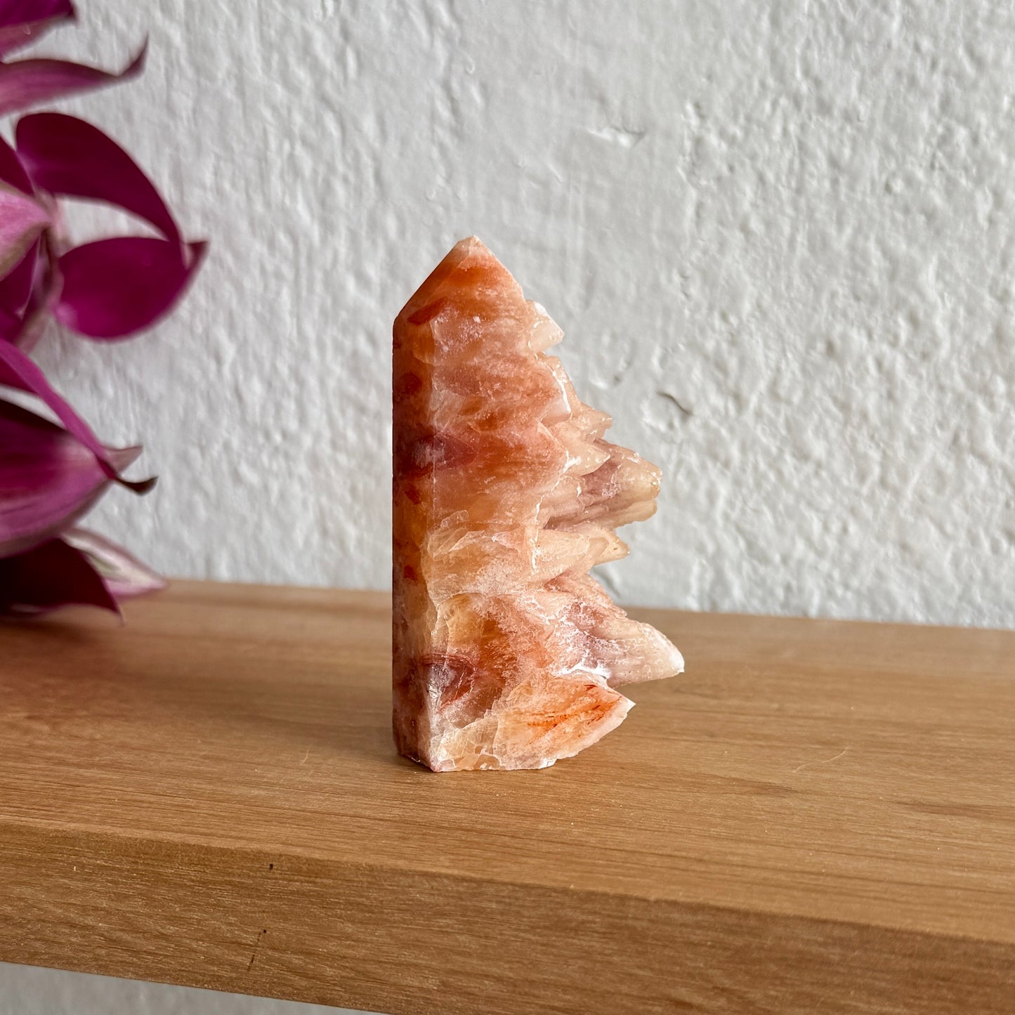 Dogtooth calcite crystal tower on a wooden surface with a white wall and purple flowers in the background
