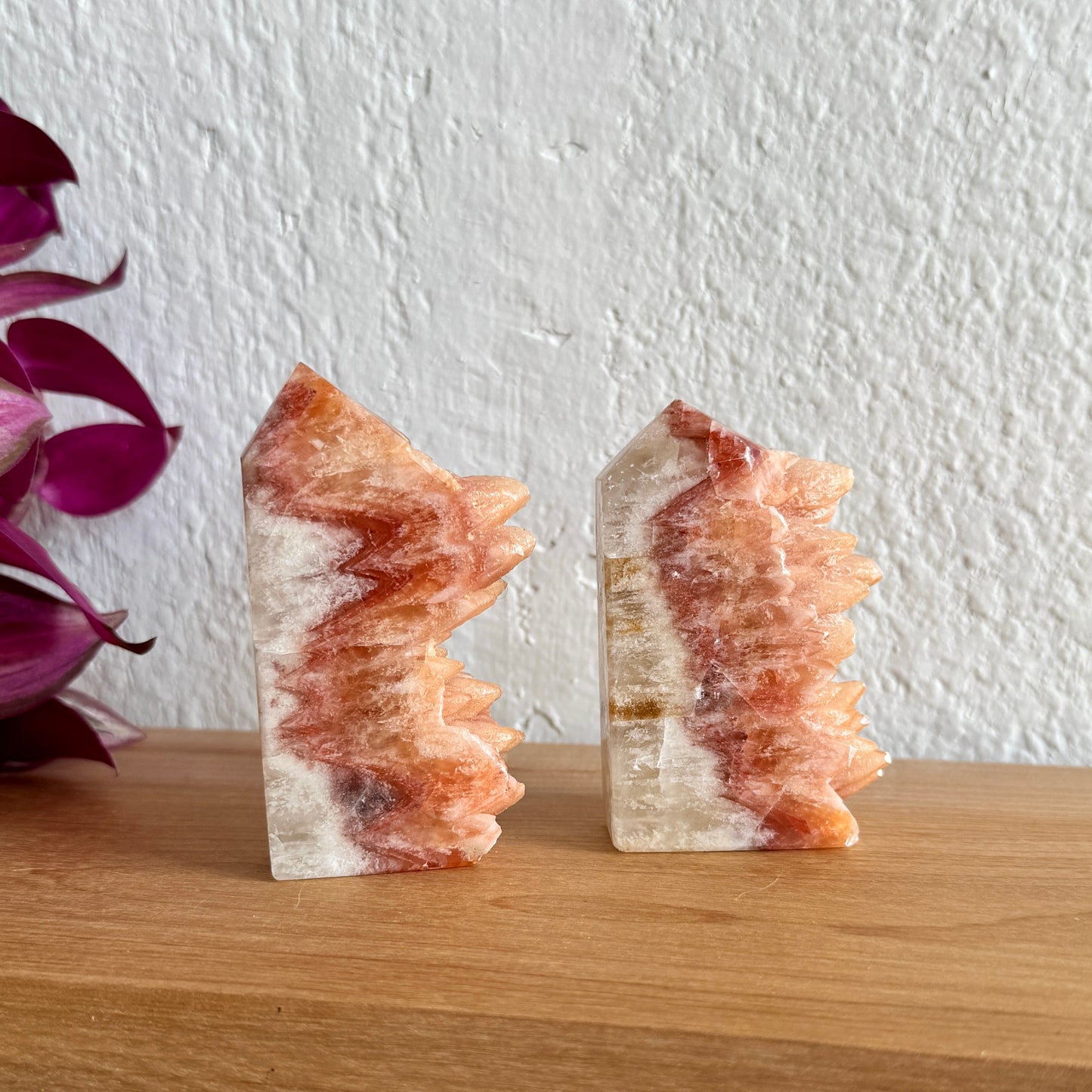 Two dogtooth crystal towers on a wooden surface with a white wall background